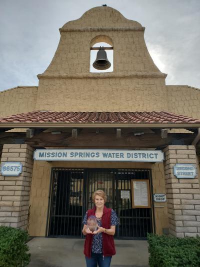 Photo of MSWD employee in front of Mission Springs Water District building holding an award.