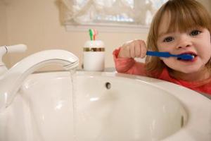 Child brushing their teeth at the sink with the water running